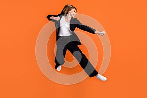 Profile side photo of young beautiful funky smiling woman doing karate fight kick isolated on orange color background