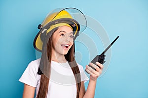Profile side photo of young girl happy positive smile wear helmet hold walkie talkie urgency isolated over blue color