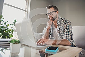 Profile side photo of young handsome man serious think look browse internet laptop sit couch home remote work