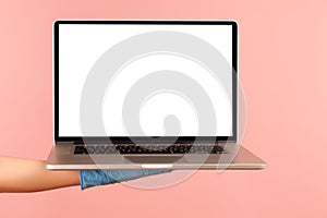 Profile side view closeup of human hand in blue surgical gloves holding computer laptop and showing empty copy space on monitor