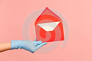 Profile side view closeup of human hand in blue surgical gloves holding red opened letter envelope