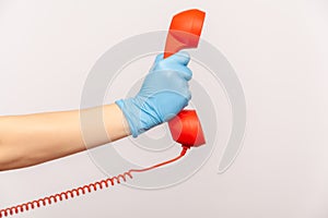 Profile side view closeup of human hand in blue surgical gloves holding and showing red cale telephone handset receiver