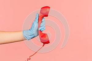 Profile side view closeup of human hand in blue surgical gloves holding and showing red call telephone handset receiver