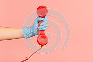 Profile side view closeup of human hand in blue surgical gloves holding and showing red call telephone handset receiver