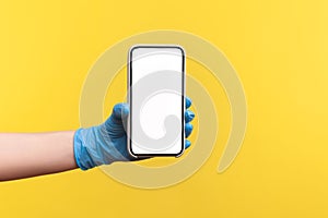 Profile side view closeup of human hand in blue surgical gloves holding and showing smart phone empty vertical display