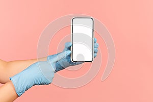 Profile side view closeup of human hand in blue surgical gloves holding and showing smart phone and pointing at empty display