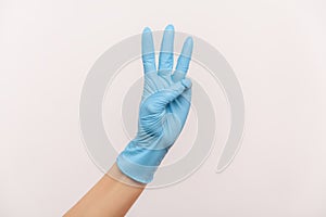 Profile side view closeup of human hand in blue surgical gloves showing number 3 with hands
