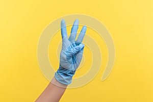 Profile side view closeup of human hand in blue surgical gloves showing number 3 three with hands