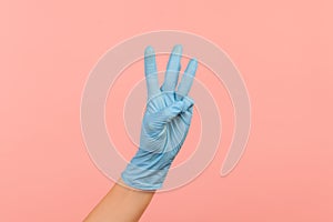 Profile side view closeup of human hand in blue surgical gloves showing number 3 three with hands