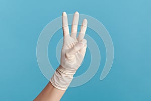 Profile side view closeup of human hand in white surgical gloves showing number 3 three with hands