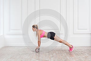 Profile side view portrait of athletic blonde young woman in fit wear using foam roller in gym to workout to loss weight and doing