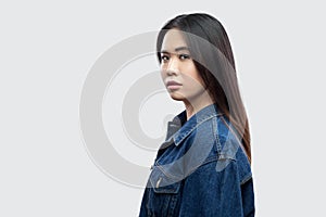 Profile side view portrait of calm serious beautiful brunette asian young woman in casual blue denim jacket with makeup standing
