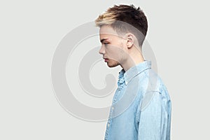 Profile side view portrait of calm serious handsome young man in light blue shirt standing and looking forward with serious face