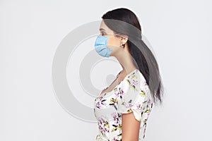 Profile side view portrait of calm young woman with medical mask in white dress standing . Protection against contagious disease,