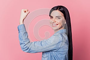 Profile side view portrait of cute cheerful girl showing strong arm muscle isolated on pink pastel color background