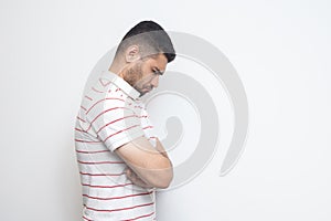 Profile side view portrait of sad alone o depressed bearded young man in striped t-shirt standing, holding his head down and