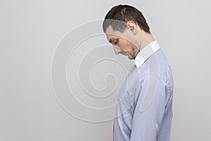 Profile side view portrait of sad depressed handsome bristle businessman in classic blue shirt standing holding head down and