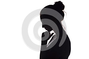 Profile silhouette of a sad girl with a hand at the chin, a young woman lowered her head and praying to God