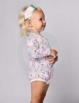 Profile of small cute blonde smiling baby girl in floral jumpsuit with flower decoration in hair