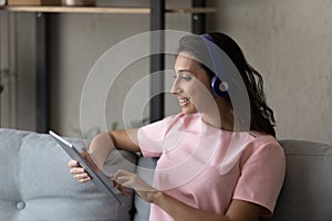 Profile of smiling Arabian woman in headphones using tablet