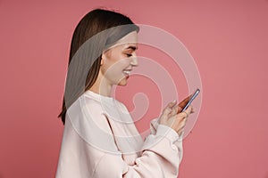 Profile of smiling woman using mobile phone while standing isolated over pink background