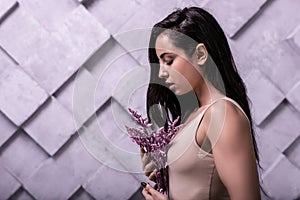 Profile studio photo of long-haired brunette girl cuddling lilac flowers