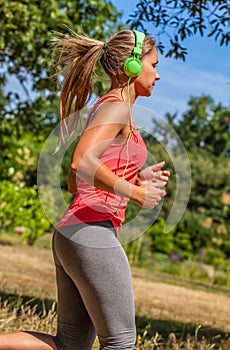 Profile of trendy young woman running listening to music in park