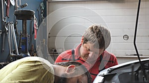 Profile of two mechanics works with car at garage. Portraits of repairmans fixing vehicle at workshop or service. Men