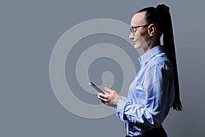 Profile view 30s woman using smartphone on grey background