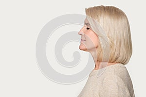 Profile view aged woman standing aside on grey studio background