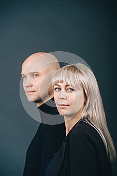 Profile view of bald man and blonde woman standing looking in same direction in studio