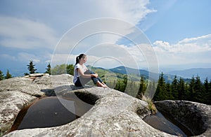 Young woman resting on a big stone in the summer day in the Carpathian mountains