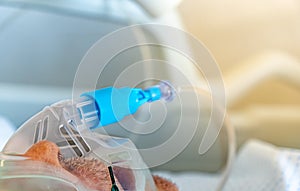 Profile view of the face of an elderly man in a hospital bed wearing a respiratory medical system oxygen mask to troubleshoot