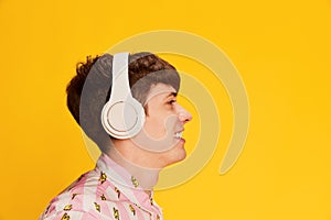 Profile view of happy young man in headphones smiling, listening to music isolated over bright yellow background. Youth