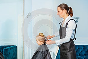 Profile view through mirror of hairdresser make haircut to a boy