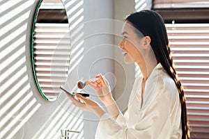 Profile view of pretty korean woman applying makeup in bathroom