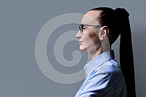 Profile view of 30s serious woman, gray background, copy space