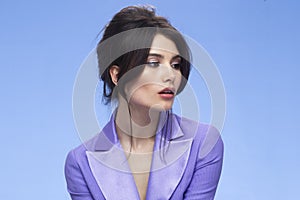 Profile view of a sexy brunette in a stylish purple suit in attractive, looking at camera, isolated blue background.