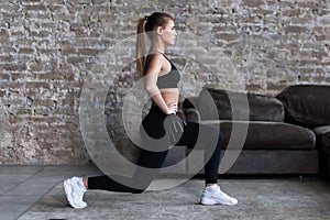 Profile view of sporty girl doing lunges working-out leg muscles and glutes in loft interior