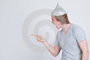 Profile view of stressed young man with tinfoil hat pointing finger and looking angry
