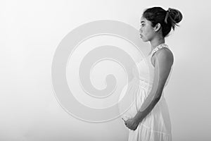 Profile view of young Asian pregnant woman holding the baby in her stomach against white background