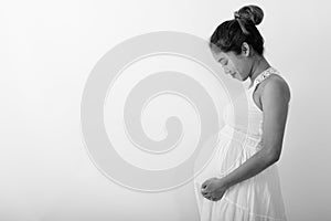 Profile view of young Asian pregnant woman holding while looking at her stomach against white background