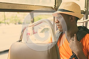 Profile view of young black African tourist man thinking and looking outside the window while riding the bus in Bangkok