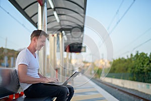 Profile View Of Young Happy Tourist Man Using Laptop At The Train Station