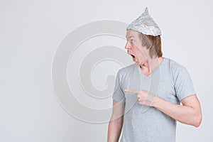 Profile view of young man with tinfoil hat pointing to side and looking shocked