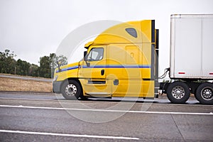 Profile of yellow big rig semi truck with semi trailer running o