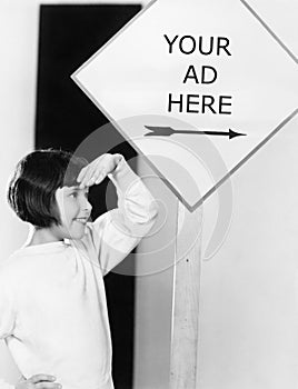 Profile of a young girl shielding her eyes under an information board