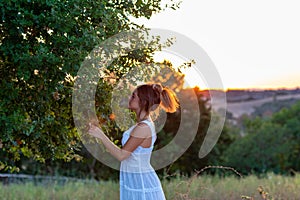 Profile of a young girl in white dress at sunset with blond tied hair near the magic tree