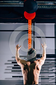 Profile of a young male athlete crouched doing wall balls exercises at the gym