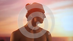 Profile of a young man with bare torso admiring a sunset, his face illuminated by the warm golden light of the twilight